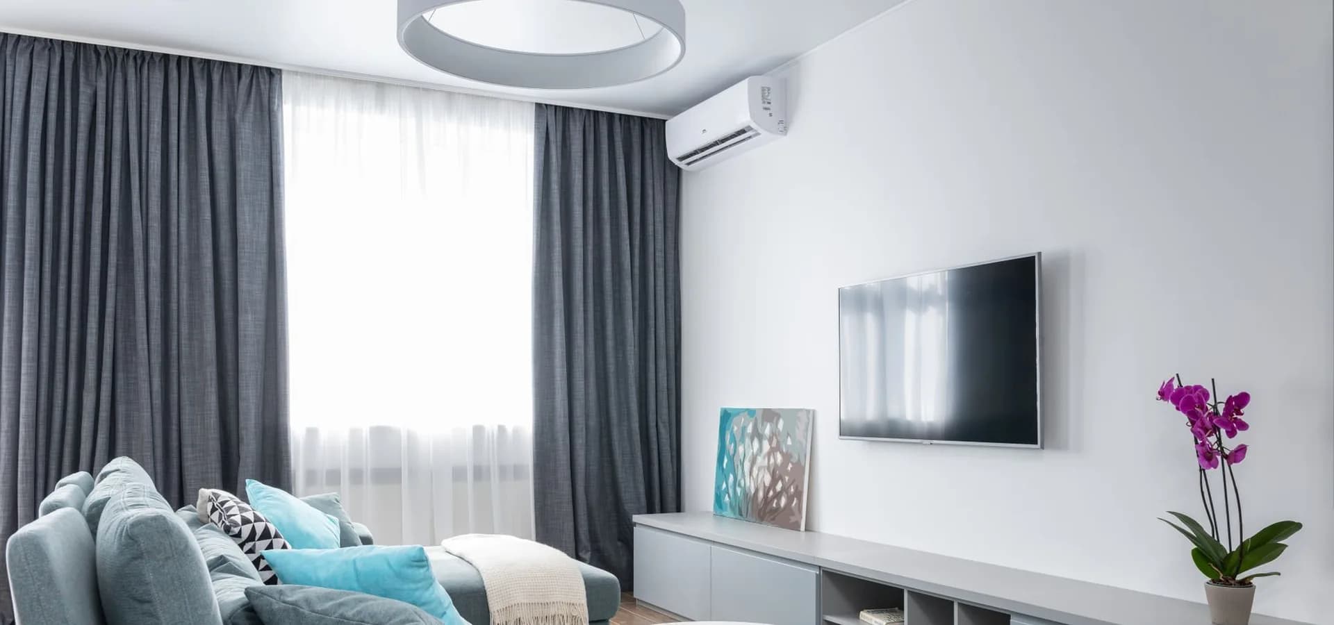 Living luminoso con aire acondicionado split en la pared, televisor y sillón celeste