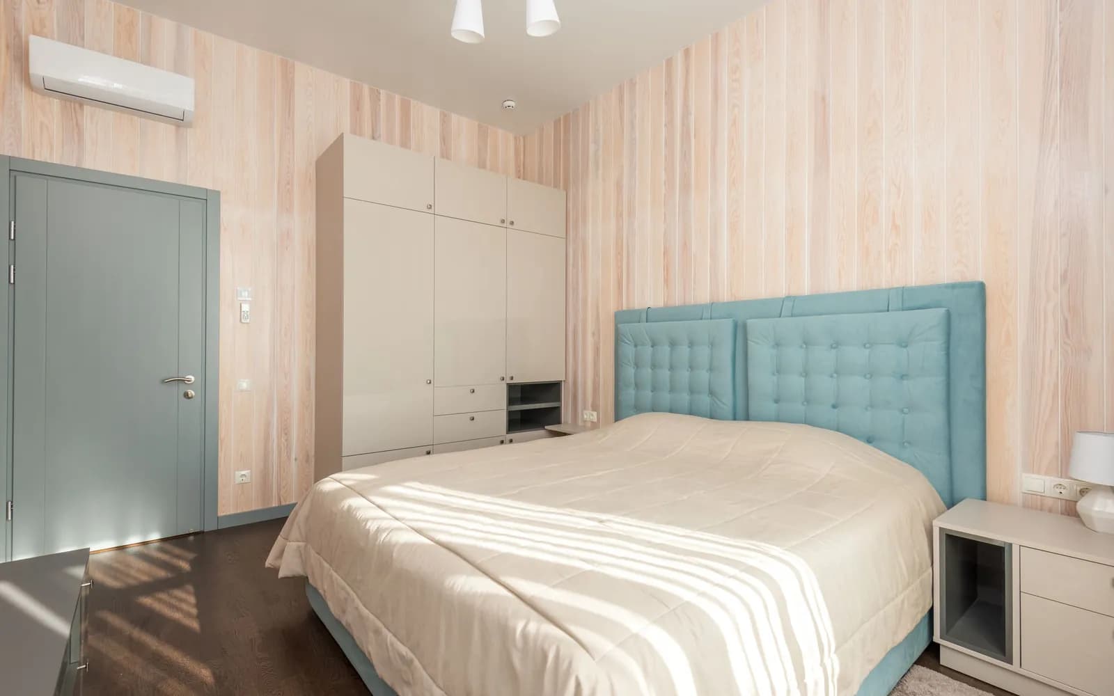 Dormitorio con aire acondicionado split sobre la pared, cama con cabecera tapizada, placar y mesa de luz