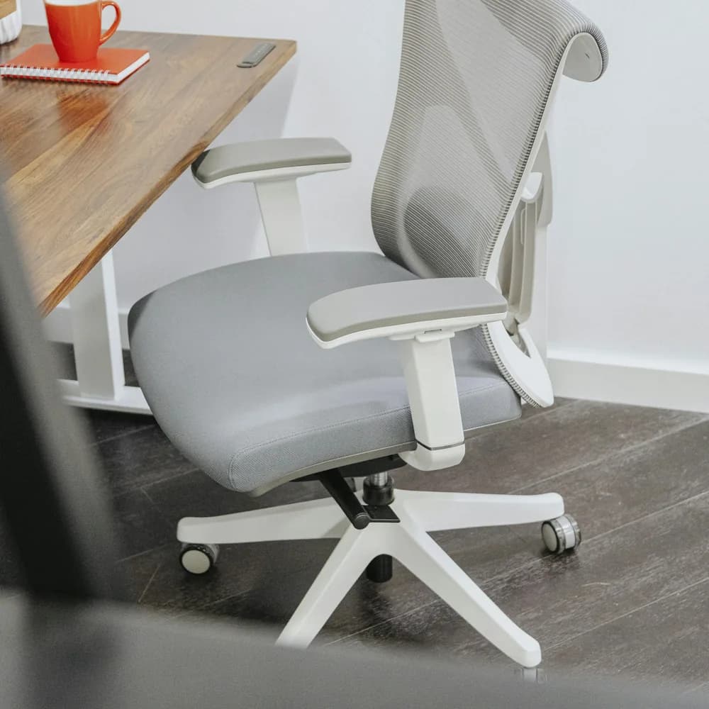 Silla de oficina gris con apoyacabezas y apoyabrazos regulables junto a un escritorio de madera